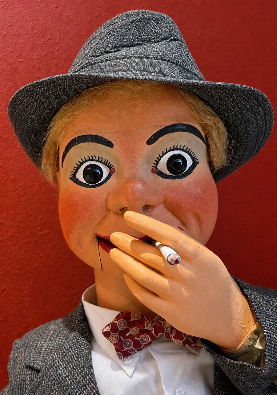 Dusty Backlog: a Mack ventriloquist figure in a grey fedora, holding a cigarette